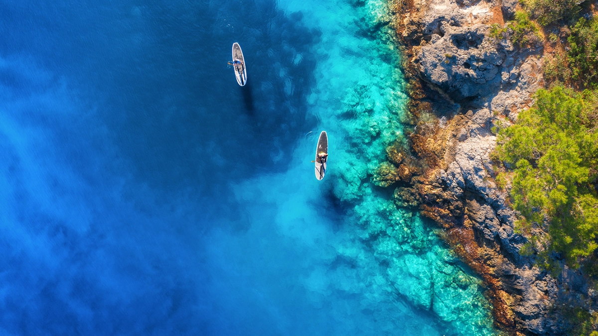 Two people paddling boats near a coast