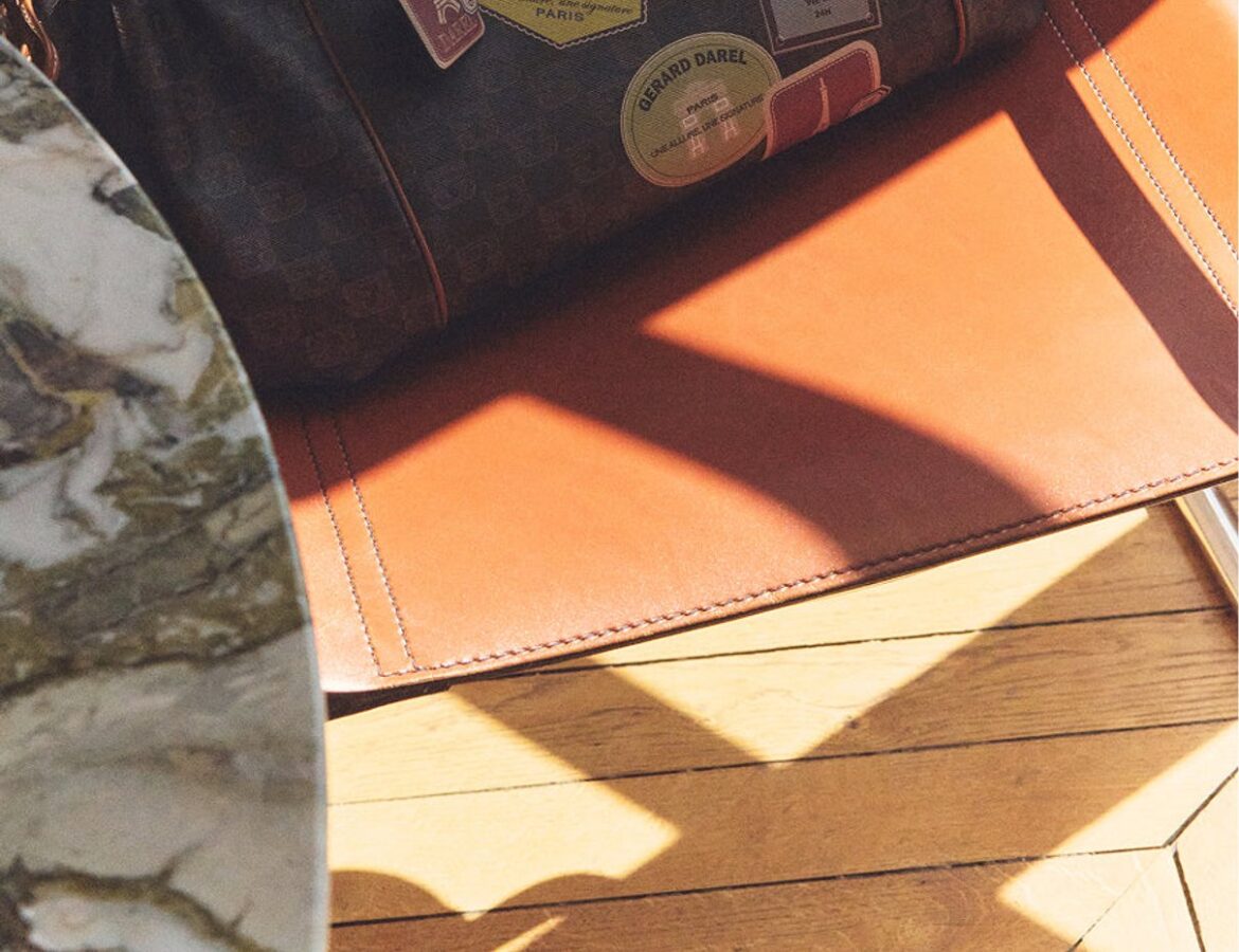 Sac 24H Gerard Darel en toile enduite et cuir avec patchs posé sur un fauteuil