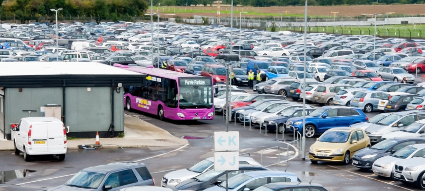 Purple shuttle bus among cars at an airport parking lot