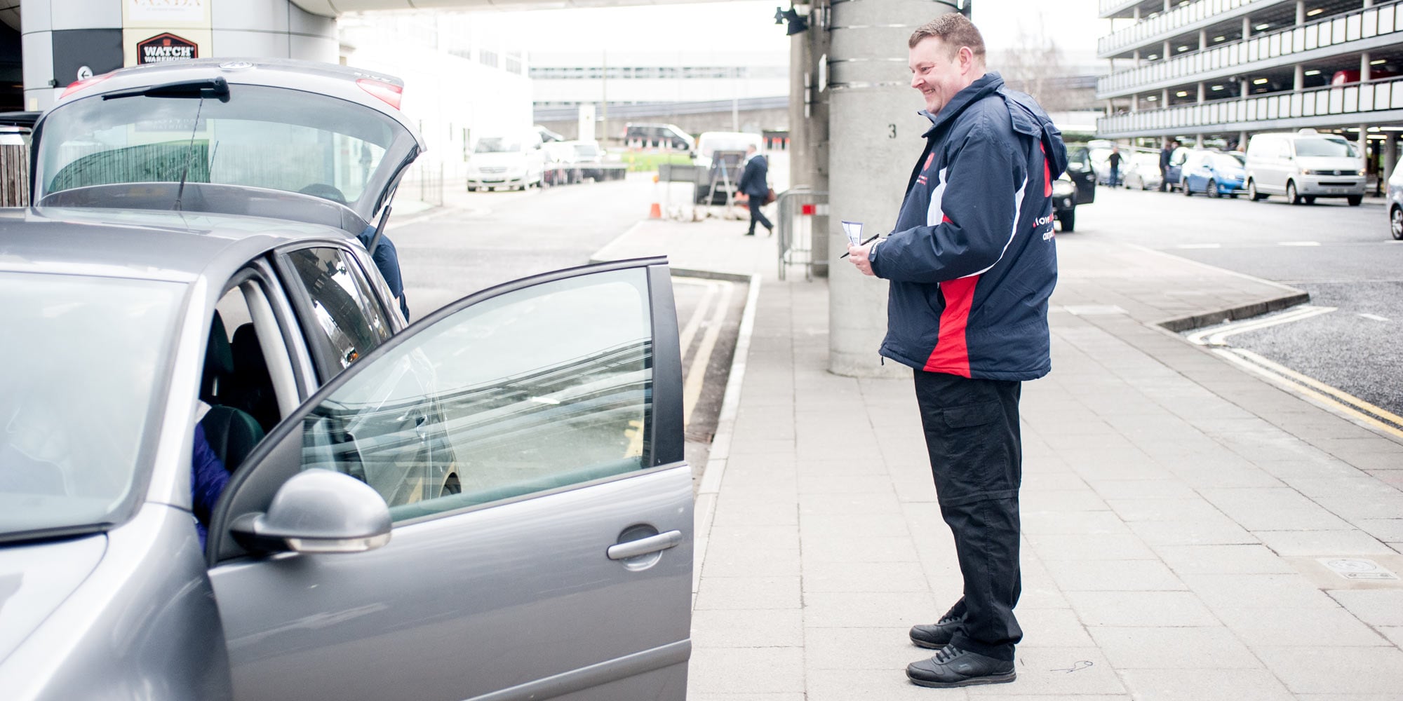 Valet attendant beside an open car at an airport forecourt