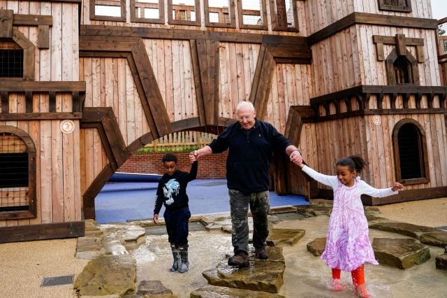 Adult helping two children cross stepping stones beneath a timber play castle