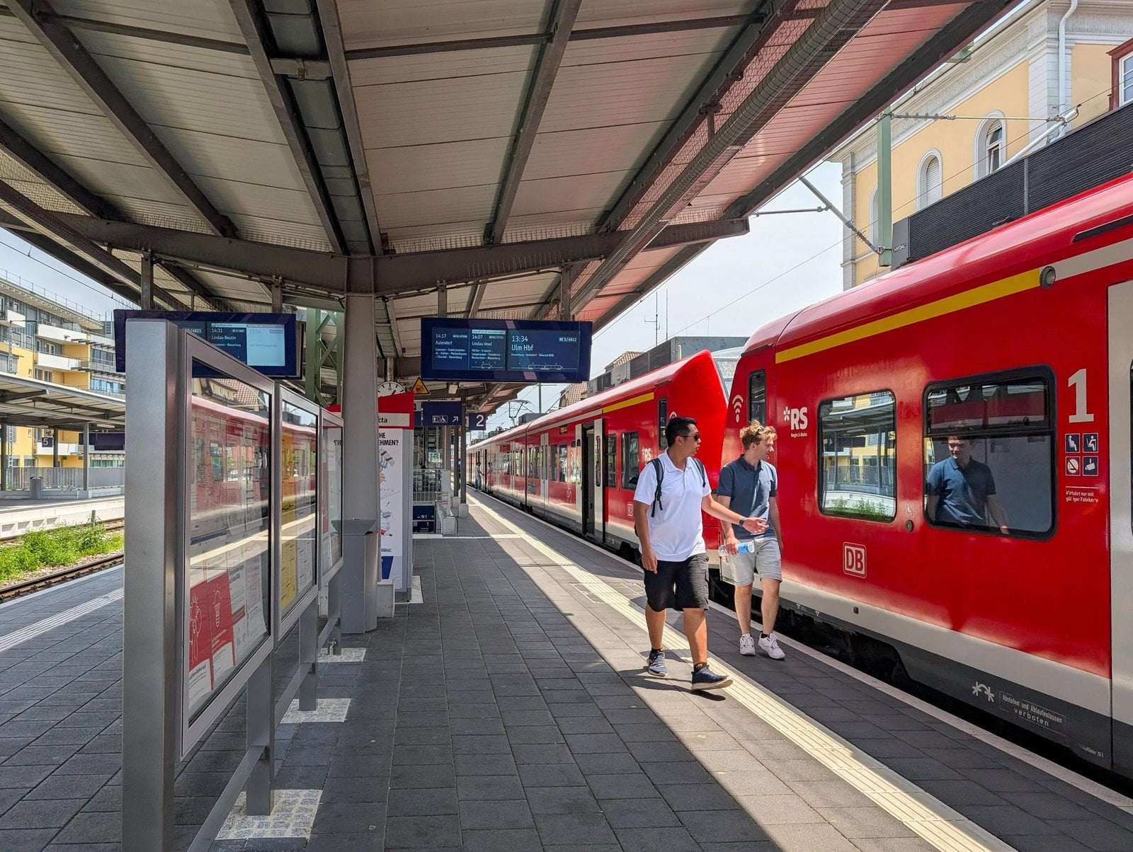 Zwei Reisende gehen an einem roten Regionalzug entlang des Bahnsteigs