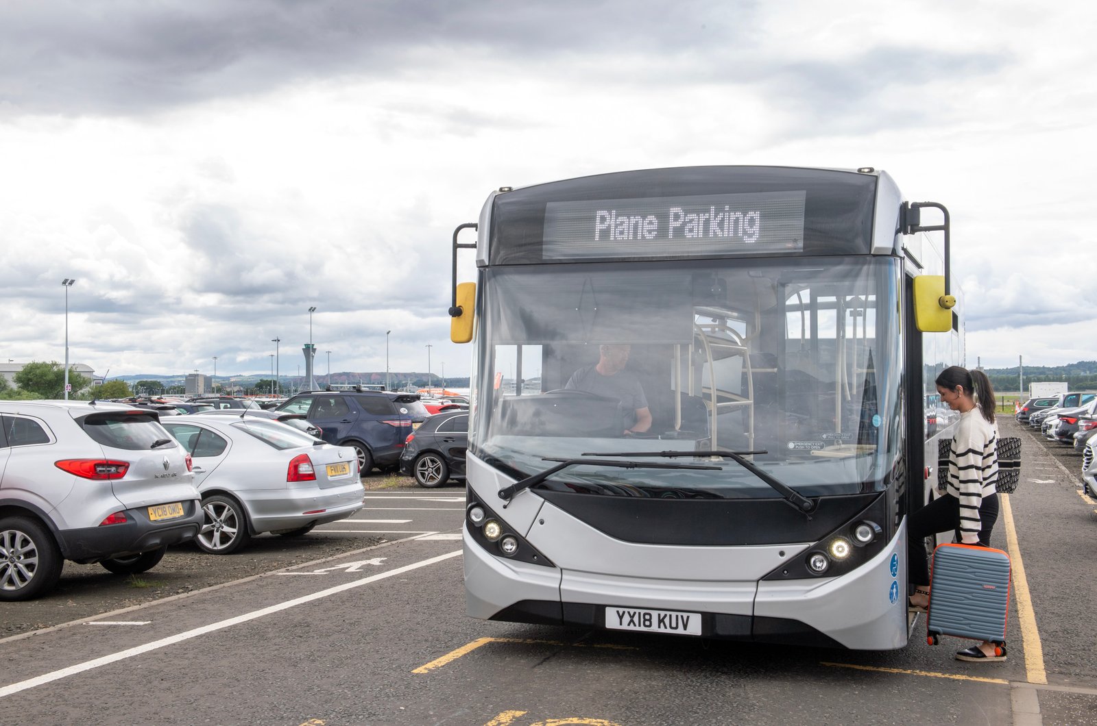 Passenger beside an airport parking shuttle and parked cars
