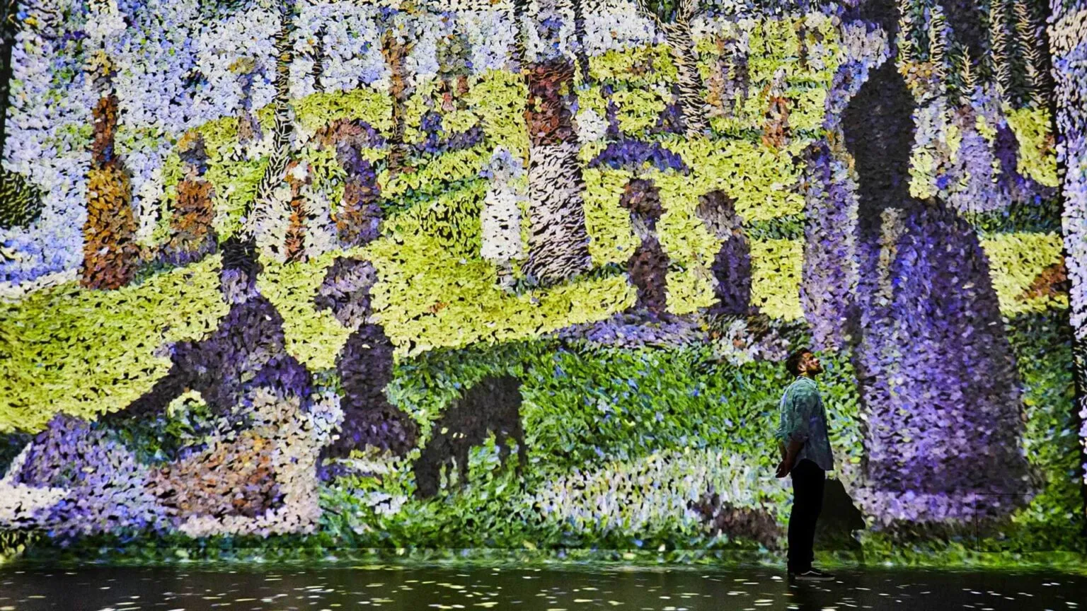 A visitor looks into a room filled with projected pointillist colour