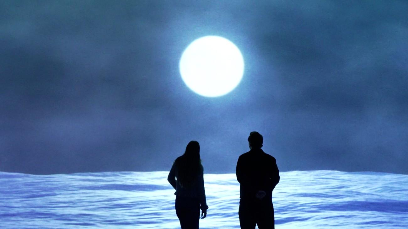 Visitors facing a moonlit projection in a Frameless gallery