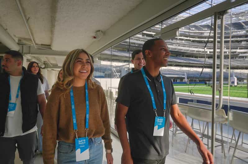 Tour visitors walking through a glass corridor overlooking the field