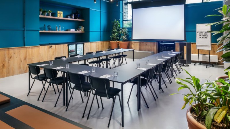 Sala de reuniones con mesa, pantalla y paredes azules